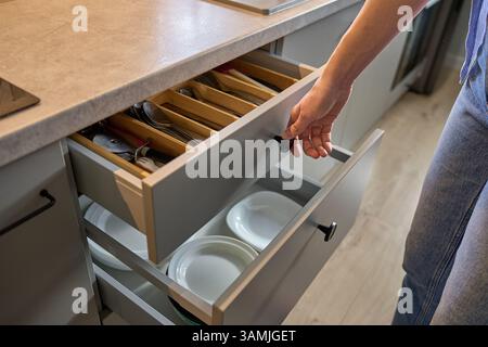 Person opens a kitchen drawer with various utensils in wooden cutlery tray. Woman opening kitchen cabinet. Concept of home organization and functionality interior Stock Photo