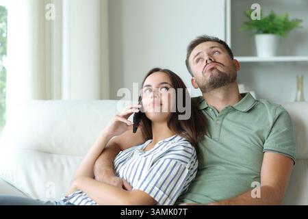 Couple talking on phone and waiting for a response sitting on a couch at home Stock Photo