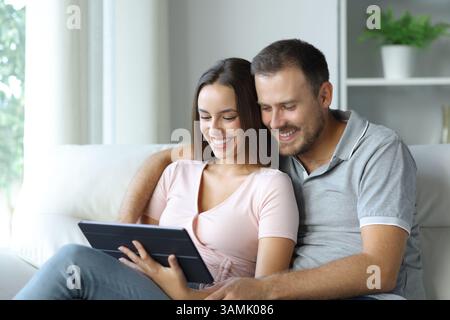 Happy couple watching online media on tablet sitting on a couch at home Stock Photo