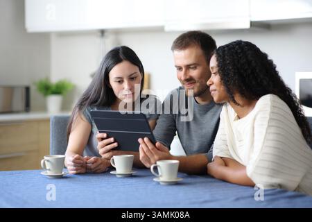 Interracial roommates watching videos on tablet in the kitchen at home Stock Photo