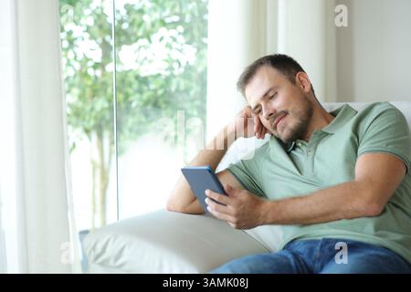 Relaxed man reading an ebook sitting on a couch at home Stock Photo