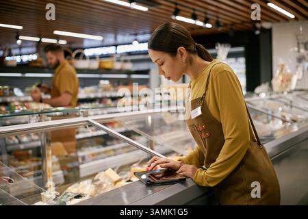Grocery store employee organizing items in refrigerated section, scanning products with handheld device in modern store environment Stock Photo