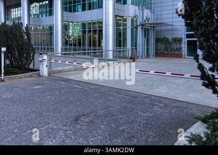 Automated parking access barriers lowered in front of a modern office building with a glass and metal facade, representing urban security systems and Stock Photo