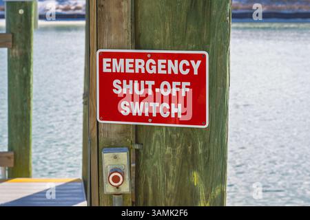 Emergency shut off switch and red and white sign mounted on utility pole at boat dock. Stock Photo