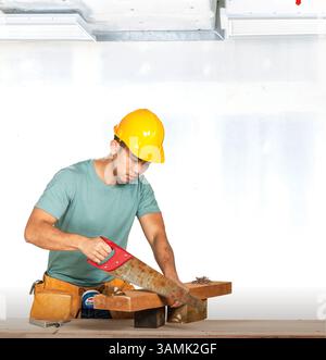 Studio portrait of a young construction worker using a rusty saw to cut wood, symbolising safety risks and labor challenges. Stock Photo