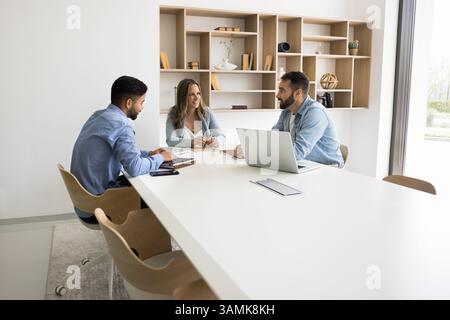 Team of three diverse multiethnic professionals gather at conference table Stock Photo