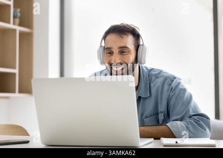 Smiling young man wear wireless headset communicate online using notebook Stock Photo
