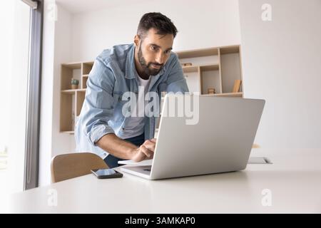 Concentrated young man leaning over work desk type on notebook Stock Photo
