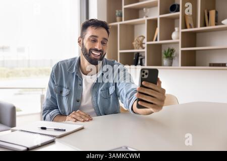 Smiling young businessman enjoy talking by videocall on cellphone Stock Photo