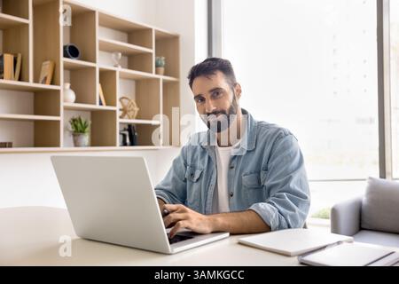 Portrait happy young man freelancer sitting at desk by notebook Stock Photo