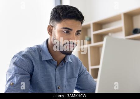 Concentrated young man looking at notebook screen taking exam remotely Stock Photo