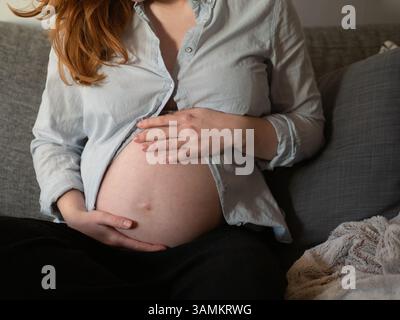 Pregnant Woman Sitting In Sofa Holding Belly Stock Photo
