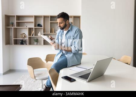 Young man remote worker reviewing paper documents at home office Stock Photo