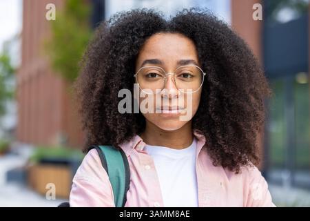 A young black woman, sporting curly hair and glasses, gazes directly at the camera, conveying a sense of calm confidence. Stock Photo