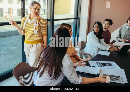 College lecturer leads a discussion with engaged students in a city classroom, emphasizing communication and teamwork. The modern setting fosters an i Stock Photo