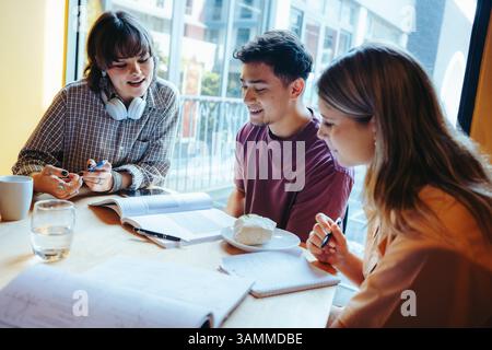 A group of classmates discussing and working on homework in a relaxed cafe setting. They are engaged and sharing ideas, surrounded by books and notebo Stock Photo