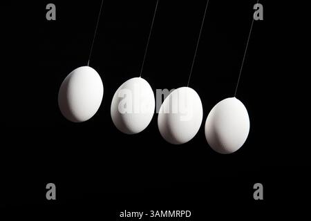 Four white eggs hang in a diagonal line against a deep black background, dramatically lit from the upper left corner. Front view. Stock Photo