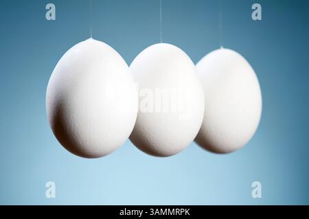 Three hanging eggs in perspective on a gradient blue background. Close up. Stock Photo