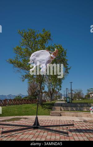 Graceful dancer in white dress performing on pole with scenic mountain and sea background Stock Photo