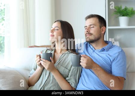 Couple smelling coffee relaxing sitting on a couch at home Stock Photo