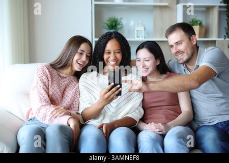 Happy group of interracial friends checking media on phone sitting at home Stock Photo