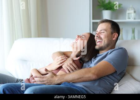 Funny couple laughing together sitting on a couch at home Stock Photo