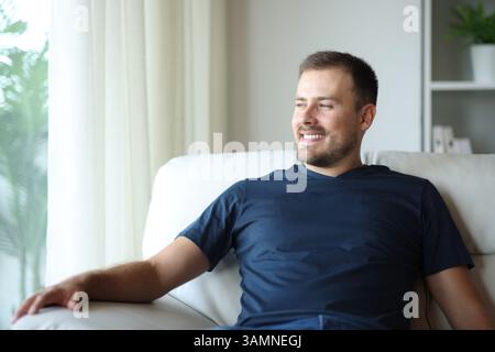 Happy man at home looking through a window sitting on a sofa Stock Photo