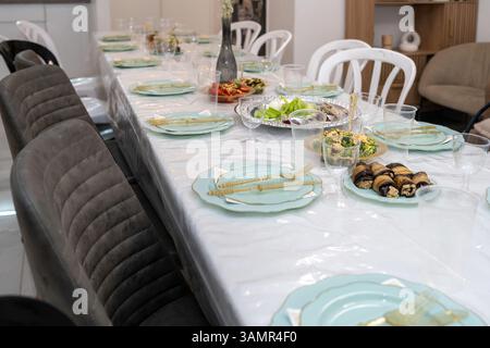 A beautifully arranged dining table awaits guests, adorned with delicate plates and glasses. A variety of dishes showcase vibrant food, creating a warm atmosphere for celebration. Stock Photo