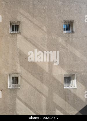Four small windows with bars and sun reflections on a light brown plastered wall Stock Photo