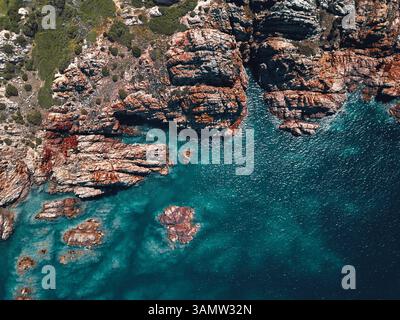 Aerial view of a breathtaking and wild coastline characterised by reddish cliffs and a turquoise transparent sea in Isola Rossa, Sardinia, Italy. Stock Photo