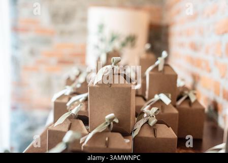 Small, neatly wrapped gift boxes with ribbons sit on a rustic table against a brick wall, suggesting a celebration or event preparation. Stock Photo