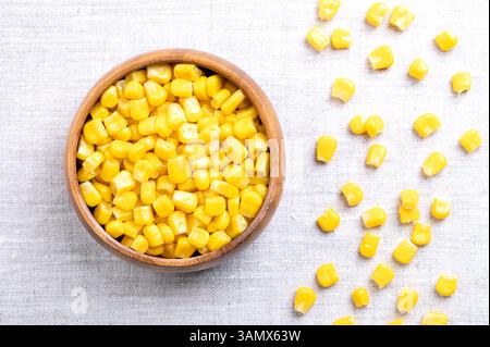 Canned vegetable maize, whole sweet corn kernels in a wooden bowl on linen. Variety of corn that is picked when in its milk state. Stock Photo