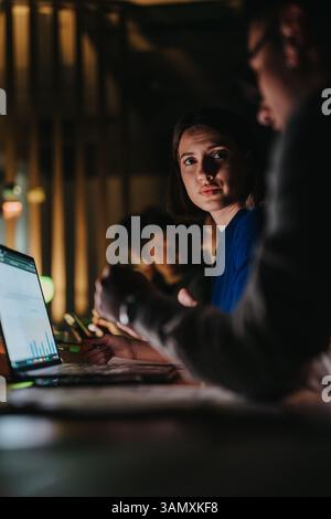 A diverse group of coworkers collaborates intensely on a project in a dimly lit office. Stock Photo