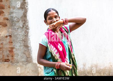 Portrait of a smiling woman decorated with nose rings and jewelry standing in front of a colorful mud wall in Orissa, India Stock Photo