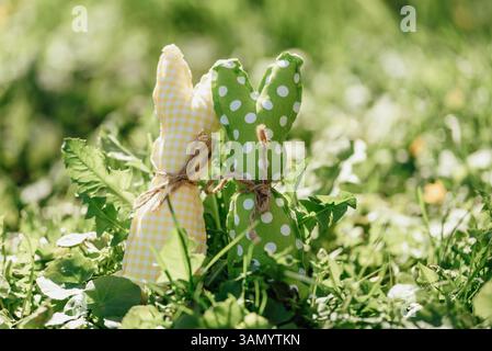 Handmade fabric Easter bunnies in yellow and green placed on vibrant green grass under bright spring sunlight Stock Photo