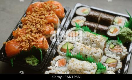 Closeup of sushi rolls with salmon avocado and crunchy topping in plastic takeaway containers for a delicious japanese meal Stock Photo