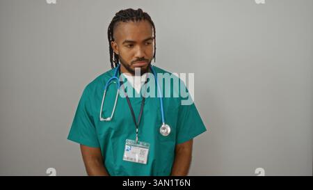 Young man in green scrubs with stethoscope stands against white wall conveying professionalism and confidence in healthcare setting Stock Photo