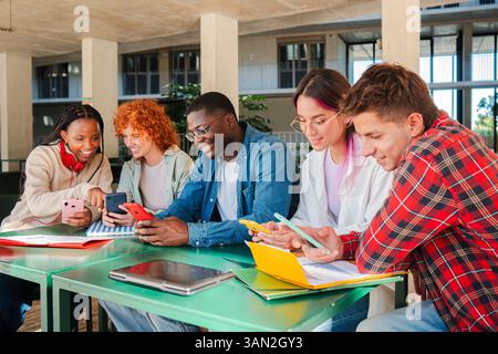 Diverse group of university students collaborating on their studies and sharing information through smartphones and laptops, showcasing teamwork and engagement in their academic pursuits and learning. High quality photo Stock Photo