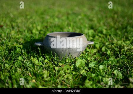 Old soviet style pot with two handles used on furnace. Vintage iron metal dish on green grass. Stock Photo