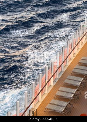 Sun loungers on cruise ship deck with sea and waves passing by, sunset Stock Photo