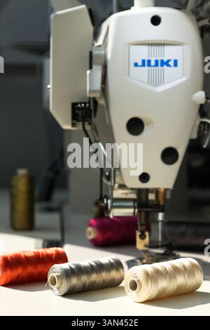 Close-up of spools of metallic colour threads laying on the white table in front of industrial sewing machine. Stock Photo