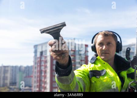 Professional Window Cleaner Using a Squeegee to Ensure a Pristine View from a Height in a Bright Urban Setting Stock Photo