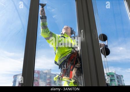 Professional Window Cleaner Performing His Job Safely While Suspended at Height, Showcasing the Importance of Safety Gear and Expertise in Window Stock Photo