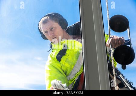 Professional Window Cleaner Safely Working at Height, Wearing Protective Gear and Using Specialized Equipment Under a Clear Blue Sky Stock Photo