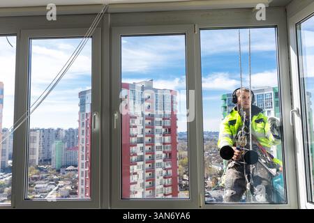 High-Rise Window Cleaner Working on a Skyscraper in a City: A View of High-Rise Apartments and Blue Sky Through Large Window Glass Panels Stock Photo