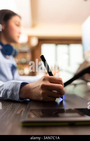Closeup of asian designer using stylus on digital drawing pad to fine tune and edit photos. Selective focus on individual adjusting color balance with graphic tablet, enhancing images for magazine use Stock Photo