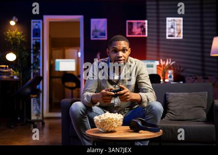Young guy having fun with video games on television modern setup, connecting his console on smart tv in living room and enjoying chill game night at home. African american gamer playing tournament. Stock Photo