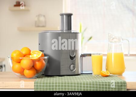 Modern juicer with oranges on table in kitchen Stock Photo