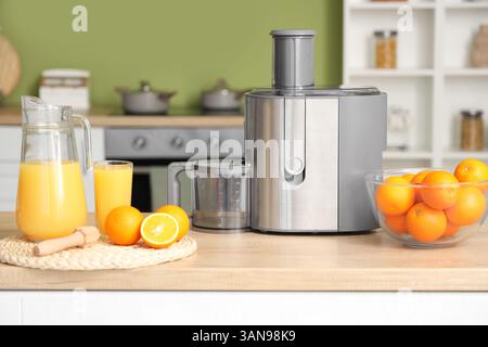 Modern juicer with fresh oranges on table in kitchen Stock Photo