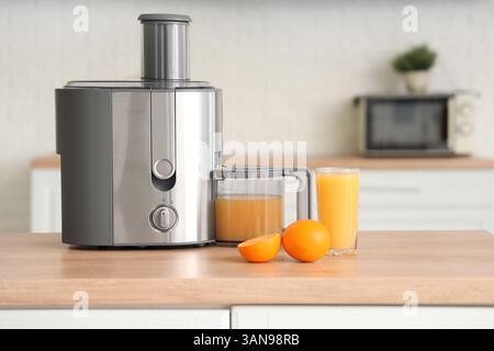 Modern juicer with fresh oranges on table in kitchen Stock Photo